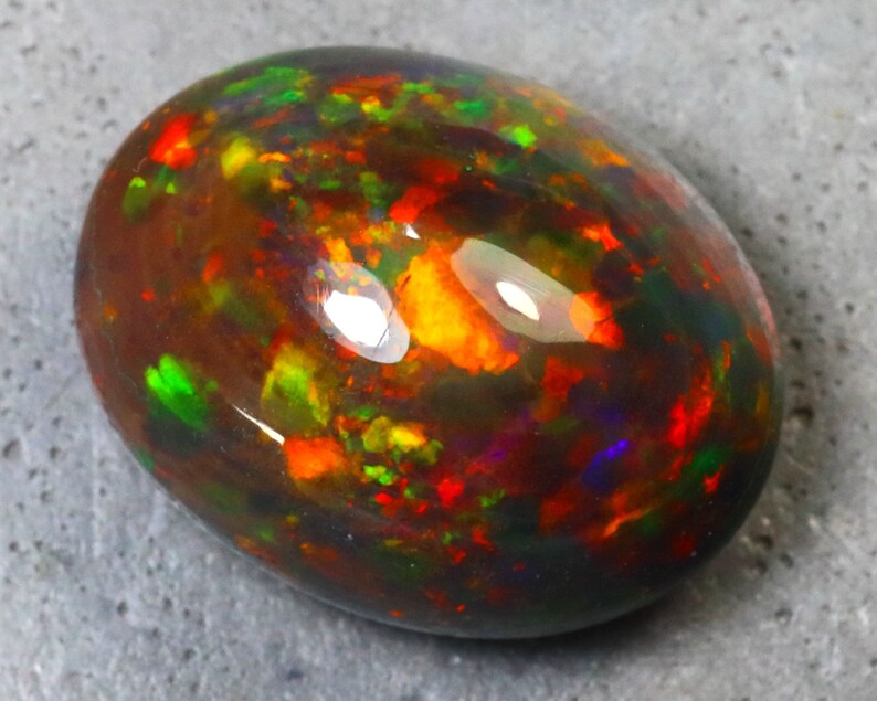 K&ouml;nnte beinhalten: Ein schwarzer Opal-Edelstein mit einem Cabochon-Schliff. Der Opal zeigt eine Vielzahl von Farben, darunter Rot, Orange, Gr&uuml;n und Lila.