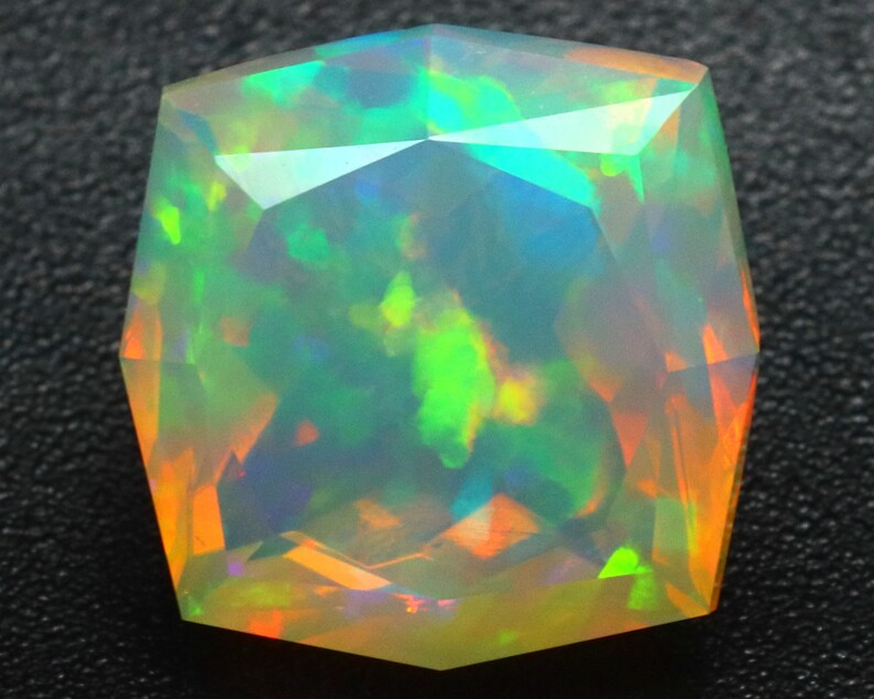 Op de afbeelding: Een levendige, veelkleurige opaal edelsteen met een gefacetteerde, kussen-vormige snede. De opaal vertoont een scala aan kleuren, waaronder groen, blauw, oranje en rood.
