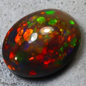 K&ouml;nnte beinhalten: Ein schwarzer Opal-Cabochon mit dunklem Hintergrund und Schimmern in Rot, Gr&uuml;n und Blau.