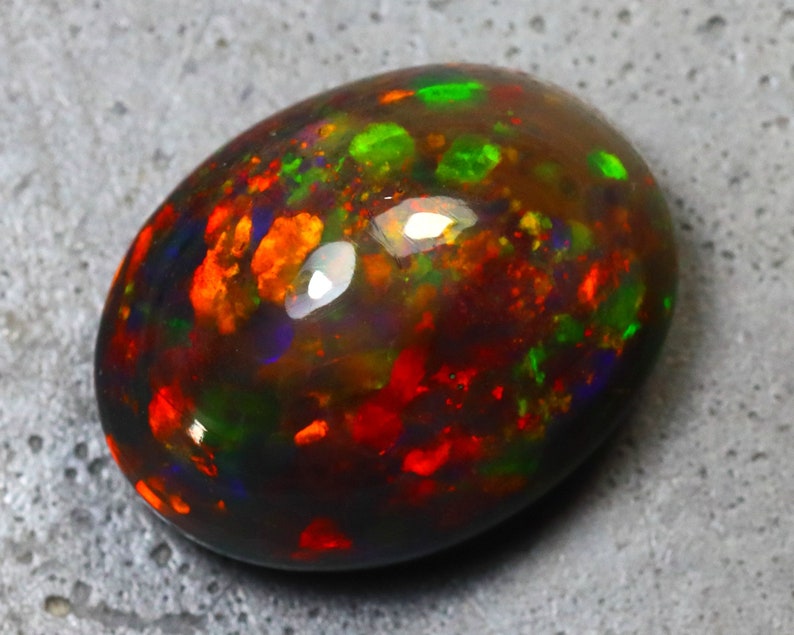 K&ouml;nnte beinhalten: Ein schwarzer Opal-Cabochon mit dunklem Hintergrund und Schimmern in Rot, Gr&uuml;n und Blau.