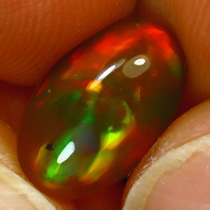 May include: A vibrant, oval-shaped opal gemstone with a fiery red, green, and yellow play of color. The opal is set against a soft, orange background.