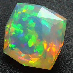 Op de afbeelding: Een gefacetteerde, iriserende opaal edelsteen met een spel van lichtgroene, oranje en blauwe kleuren. De opaal is geslepen in een hexagonale vorm en heeft een doorschijnende uitstraling.
