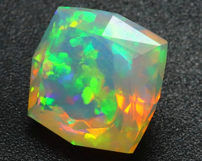 Op de afbeelding: Een gefacetteerde, iriserende opaal edelsteen met een spel van lichtgroene, oranje en blauwe kleuren. De opaal is geslepen in een hexagonale vorm en heeft een doorschijnende uitstraling.