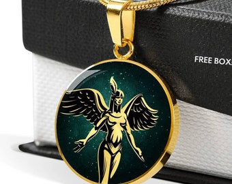 May include: Gold necklace with a round pendant featuring a stylized image of a winged woman with a feather headdress against a dark green background with gold glitter. The pendant is surrounded by a gold border. The necklace is on a black box with the text "FREE BOX!" printed on it.