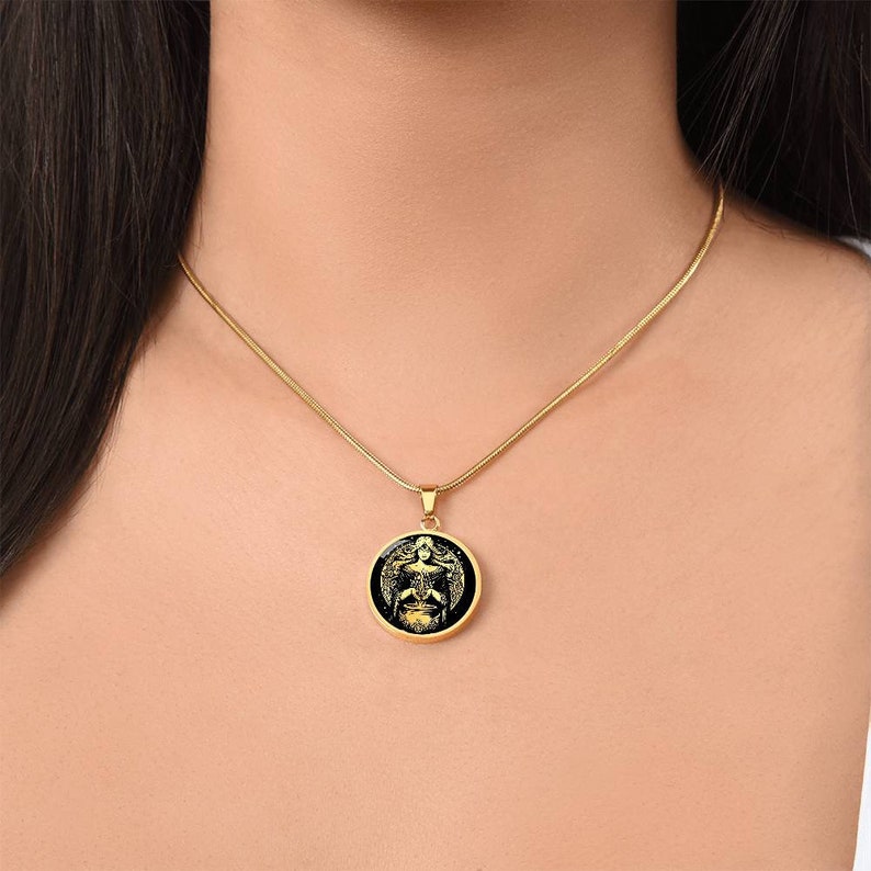 May include: A gold chain necklace with a round pendant featuring a black and gold image of a winged figure.