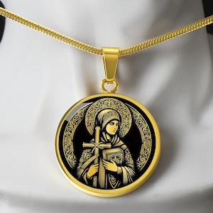 Op de afbeelding: Goudkleurige hangerketting met een religieus icoon. De ronde hanger toont een gedetailleerde illustratie van een figuur die een kruis en een boek vasthoudt, tegen een zwarte achtergrond met gouden accenten. De ketting heeft een fijne ketting.