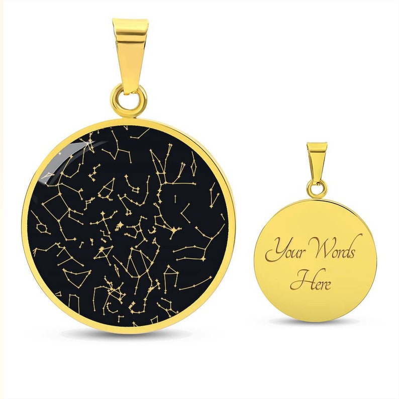 May include: Two gold-colored pendant necklaces. One pendant features a black background with a constellation design in gold. The other pendant is gold with the words "Your Words Here" engraved on it. Both pendants have a gold bail.