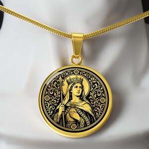 Op de afbeelding: Een goudkleurige ronde hanger met een zwart-gouden grafische illustratie van een gekroonde figuur die een staf vasthoudt. De hanger hangt aan een bijpassende goudkleurige slangenketting en toont gedetailleerde florale krulmotieven.