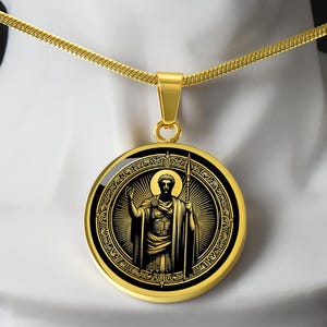 Könnte beinhalten: Eine goldene Kettenkette mit einem runden Anhänger, der ein schwarzes und goldenes Bild eines Mannes mit einem Speer zeigt. Der Anhänger hat einen dekorativen Rand.