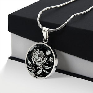 May include: A silver chain necklace with a round pendant featuring a black and white illustration of a peony flower.