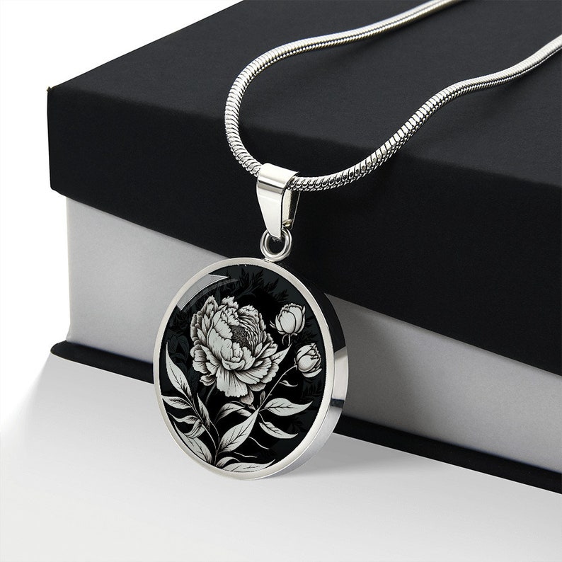 May include: A silver chain necklace with a round pendant featuring a black and white illustration of a peony flower.