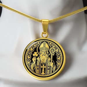 May include: A gold-toned circular pendant necklace featuring a detailed black and gold graphic of Saint Patrick holding a shamrock and a crosier. The design is framed by a circular border decorated with shamrock motifs and hangs on a gold chain.
