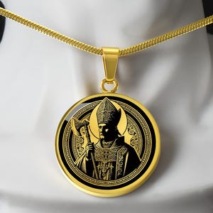 May include: Gold-toned pendant necklace featuring a detailed black and gold illustration of a figure holding an axe. The round pendant hangs from a delicate gold chain. The design includes intricate patterns and a halo effect.