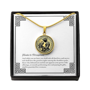 May include: A gold necklace with a round pendant featuring a black and gold illustration of Hades and Persephone. The pendant has a quote from Hades to Persephone: "And while you are here, you shall rule all that lives and moves and shall have the greatest rights among the deathless gods: those who defraud you and do not appease your power with offerings, reverently performing rites and paying fit gifts, shall be punished for evermore."