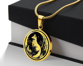 May include: A gold necklace with a round pendant featuring a black and white illustration of a fox standing in a forest setting. The pendant has a gold rim and a black background.