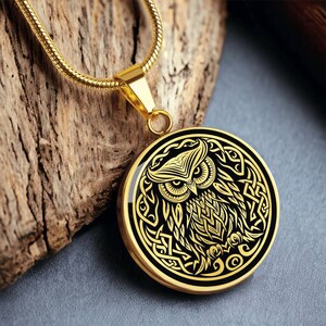 K&ouml;nnte beinhalten: Goldkette mit einem runden Anh&auml;nger, der ein schwarzes und goldenes Eulenmotiv mit keltischen Knoten zeigt.