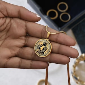 May include: Gold necklace with a round pendant featuring a black and white image of two figures embracing. The pendant has a decorative border.