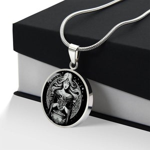 May include: A silver necklace with a round pendant featuring a black and white illustration of a woman holding a cauldron with a plant growing from it. The woman is surrounded by a circle of vines and stars.