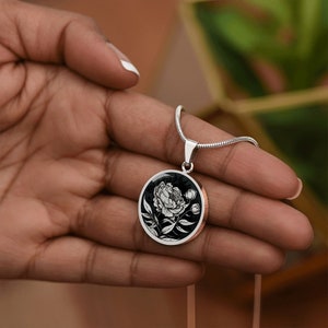 May include: A silver chain necklace with a black and white round pendant featuring a detailed illustration of a peony flower.