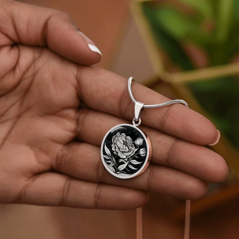 May include: A silver chain necklace with a black and white round pendant featuring a detailed illustration of a peony flower.