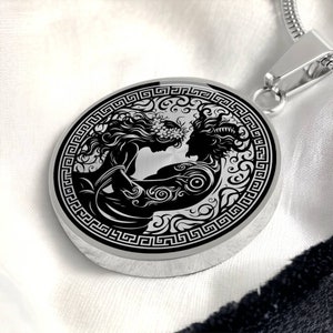 May include: A silver pendant necklace with a black and white design of two figures intertwined. The design is surrounded by a Greek key border.
