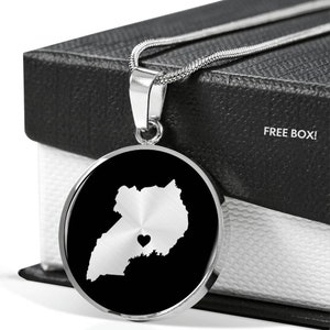 May include: A silver necklace with a round pendant featuring a black and white outline of Uganda with a small heart in the center. The necklace is displayed in a black box with the words "FREE BOX!" printed on it.