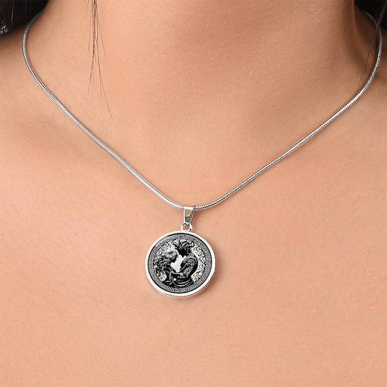 May include: A silver chain necklace with a round pendant featuring a black and white illustration of two figures embracing within a circular design.