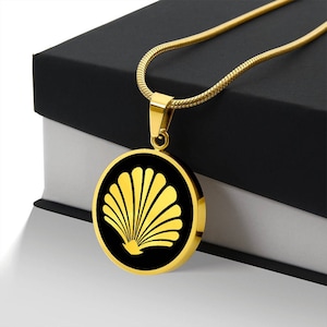 May include: A gold necklace with a round pendant featuring a black background and a gold seashell design.