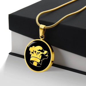 May include: A gold chain necklace with a round pendant featuring a black chef's hat design.