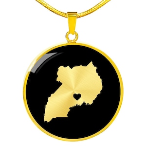 May include: Gold necklace with a round pendant featuring a black background and a gold outline of the country of Uganda with a small heart in the center.