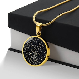 May include: Gold-toned pendant necklace featuring a circular pendant with a black background and a constellation design in gold. The necklace has a delicate chain and a simple clasp. The pendant is approximately 1.5 inches in diameter.