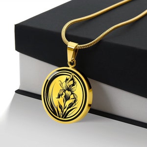 May include: A gold necklace with a round pendant featuring a black and white illustration of an iris flower. The pendant has a gold border and a black background.
