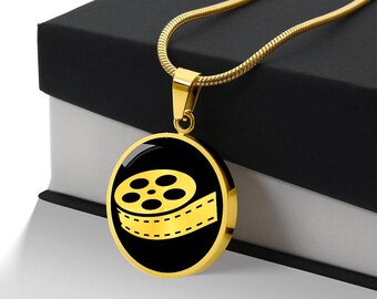 May include: A gold necklace with a round pendant featuring a black and gold film reel icon.