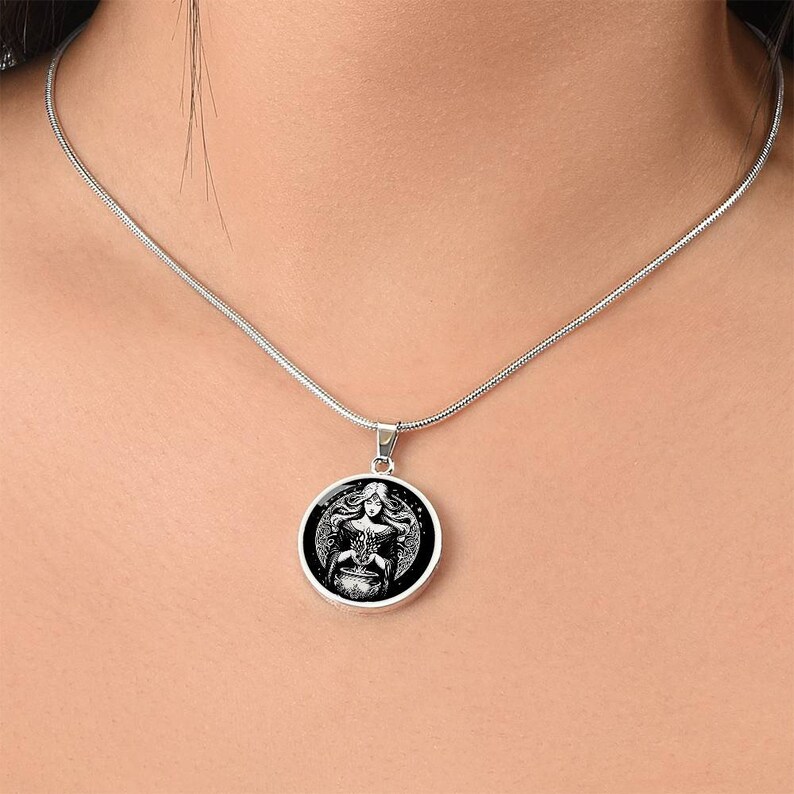 May include: A silver chain necklace with a round pendant featuring a black and white illustration of a woman holding a cauldron. The woman is surrounded by stars.