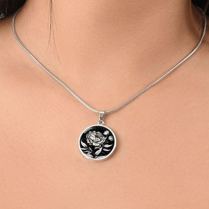 May include: A silver chain necklace with a round pendant featuring a black and white illustration of a peony flower.