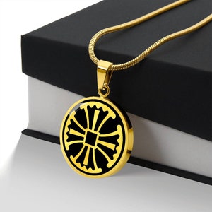 May include: A gold chain necklace with a round pendant featuring a black cross design. The pendant has a gold border and a black enamel fill.