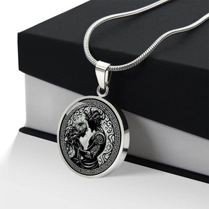 May include: A silver necklace with a round pendant featuring a black and white illustration of a couple embracing. The pendant is surrounded by a decorative border.
