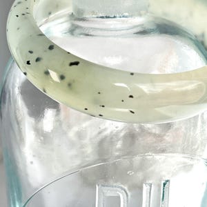 May include: A light green jade bangle with black speckles. The bangle is smooth and polished.