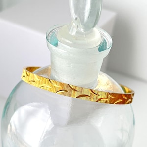 May include: A gold bangle bracelet with a textured, patterned design. The bracelet is thin and delicate.