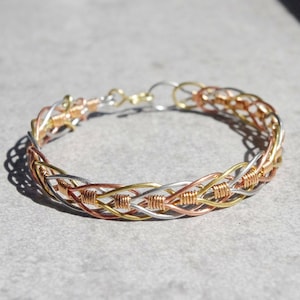 May include: A braided bracelet made of silver, gold, and copper wire.