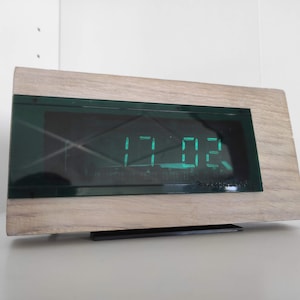 May include: A wooden digital clock with a green LED display showing the time 11:02. The clock has a black frame and the text "Snokspoor" is visible on the bottom.