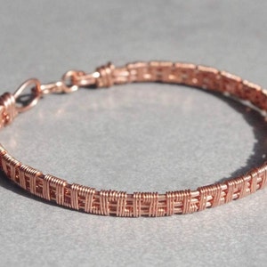 May include: A copper wire bracelet with a woven design. The bracelet is made of thin copper wire that is woven together to create a delicate and intricate pattern.