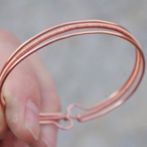 Può includere: Un braccialetto in filo di rame con un design semplice e minimalista. Il braccialetto è realizzato con due fili di filo intrecciati insieme.