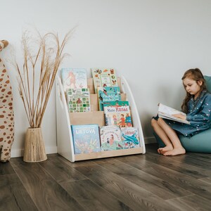 A girl reads a book sitting near floor Montessori bookshelf. As the bookshelf is designed to be placed on the floor, it is suitable for use from the youngest child up to school age.
