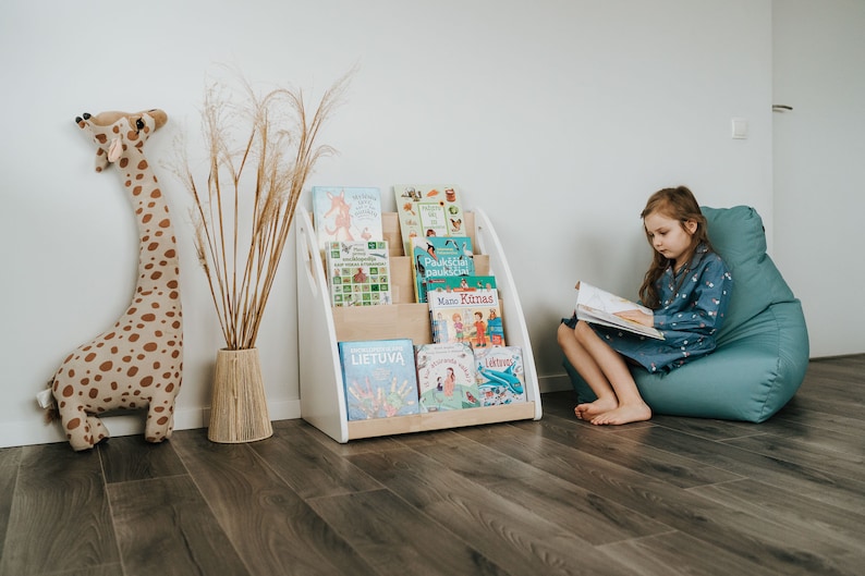 A girl reads a book sitting near floor Montessori bookshelf. As the bookshelf is designed to be placed on the floor, it is suitable for use from the youngest child up to school age.