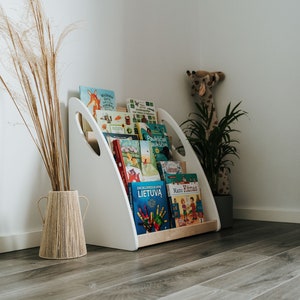 Solid wood floor Montessori floor bookshelf. All books are stored picture-forward. Side panels painted in white, middle parts oiled in clear oil. Is sturdy and robust, all corers are rounded so it is safe to use even for babies.