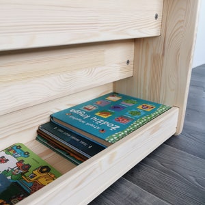 The photo shows the back of a Montessori bookshelf with storage. It is a shelf with a bottom and a low drawer that can hold about 6-10 books. The Montessori bookcase is uncoated, the natural colour of the wood is light.