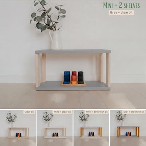 May include: A small, two-shelf wooden unit with a gray top and natural wood legs. The unit is holding a set of colorful wooden blocks. The text "MINI - 2 SHELVES" and "Grey + clear oil" is visible.