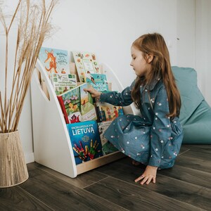 A girl takes a book from the Montessori bookshelf. As the bookshelf is designed to be placed on the floor, it is suitable for use from the youngest child up to school age.
