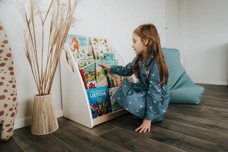 A girl takes a book from the Montessori bookshelf. As the bookshelf is designed to be placed on the floor, it is suitable for use from the youngest child up to school age.